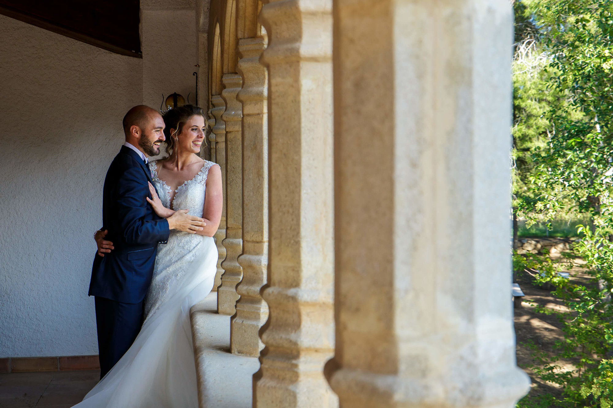 El novio y la novia miran a sus invitados desde el claustro en Masia Torreblanca.